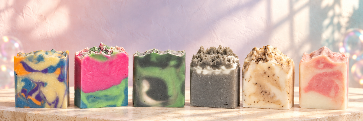 Six distinct handmade Fizze Bath soap designs on a warm stone surface with a soft pastel backdrop